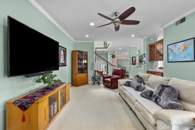 living room with visible vents, ornamental molding, stairs, ceiling fan, and light colored carpet