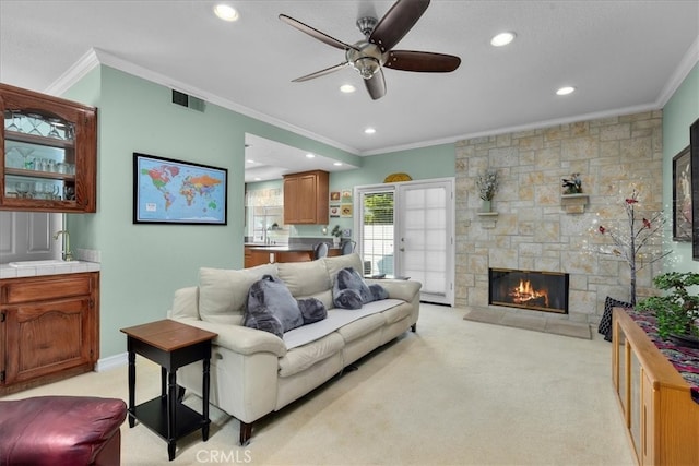 living room with crown molding, ceiling fan, light colored carpet, a fireplace, and visible vents