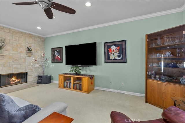 living room featuring carpet flooring, ceiling fan, a stone fireplace, baseboards, and ornamental molding