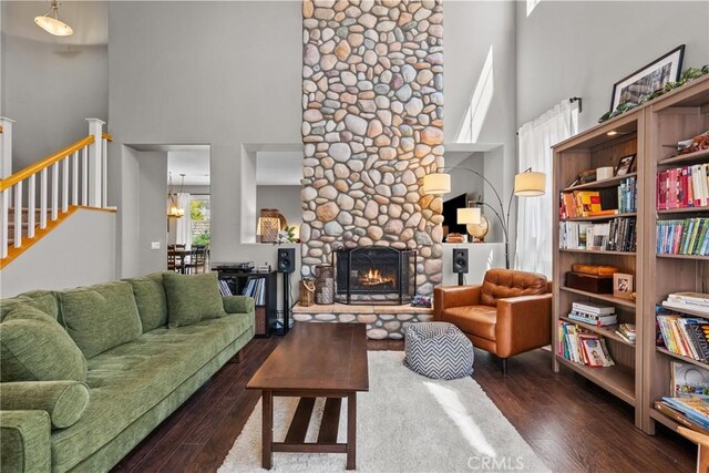 living area featuring a high ceiling, dark wood-style flooring, a stone fireplace, and stairs