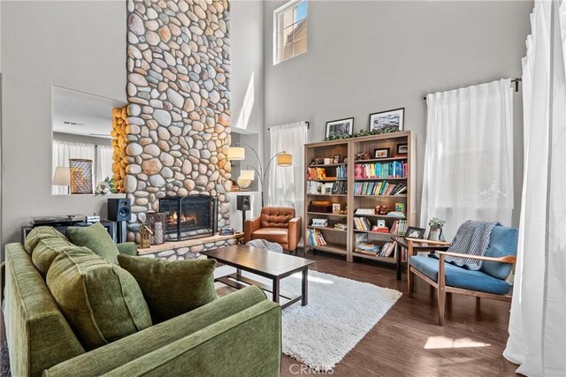 living area featuring a stone fireplace, dark wood-style flooring, a towering ceiling, and a healthy amount of sunlight