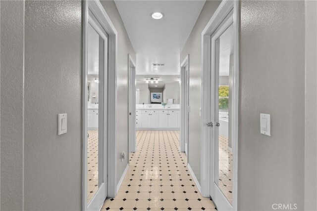 hallway featuring a textured wall, baseboards, and light floors