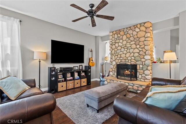 living area featuring baseboards, ceiling fan, a stone fireplace, and wood finished floors