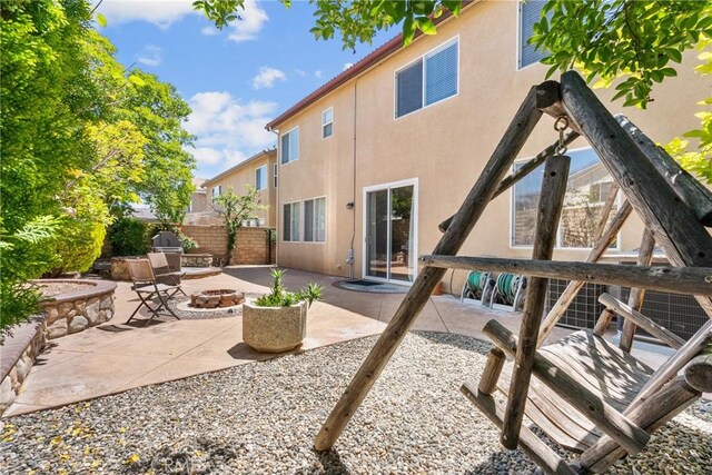 rear view of house featuring fence, a patio, stucco siding, and a fire pit
