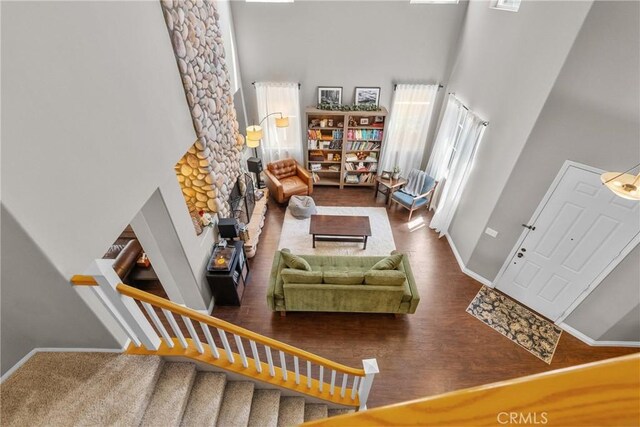 living area featuring baseboards, a high ceiling, a stone fireplace, and wood finished floors