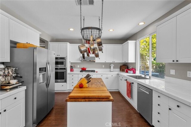 kitchen with appliances with stainless steel finishes, a sink, a center island, visible vents, and butcher block counters