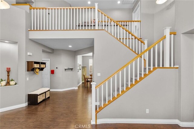 stairs with wood finished floors, recessed lighting, baseboards, and a high ceiling