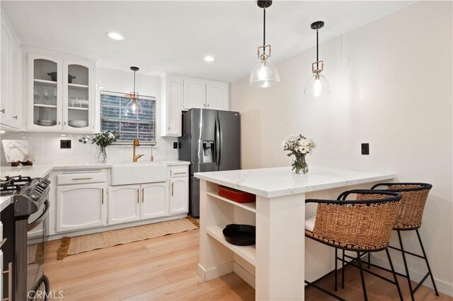kitchen featuring range with gas stovetop, a peninsula, white cabinets, stainless steel fridge with ice dispenser, and a sink