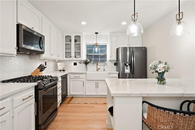kitchen featuring white cabinets, a sink, decorative light fixtures, decorative backsplash, and black appliances