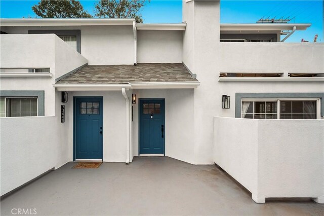 exterior space featuring a shingled roof and stucco siding