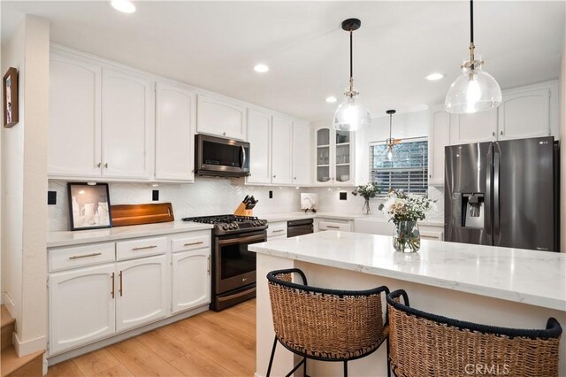 kitchen with a breakfast bar area, stainless steel appliances, white cabinetry, and backsplash