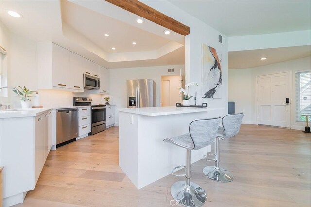 kitchen with a peninsula, a breakfast bar area, recessed lighting, light wood finished floors, and appliances with stainless steel finishes