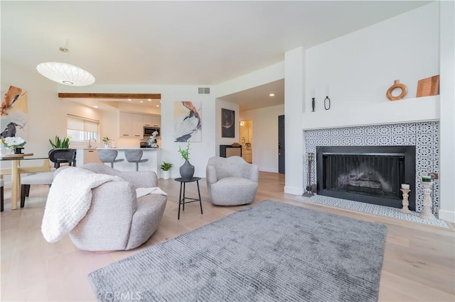 living area featuring a tiled fireplace, light wood-type flooring, and visible vents