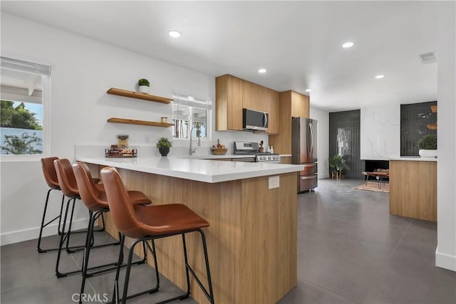 kitchen featuring plenty of natural light, a breakfast bar area, stainless steel appliances, and finished concrete floors