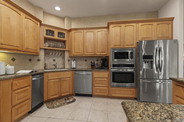 kitchen featuring stainless steel appliances, tasteful backsplash, a sink, and dark stone countertops