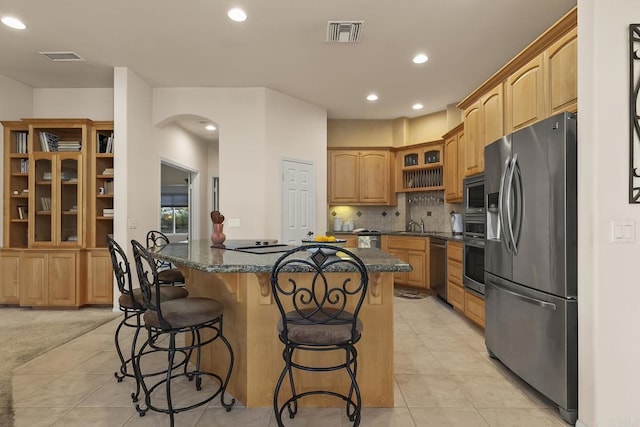 kitchen with a breakfast bar, arched walkways, stainless steel appliances, visible vents, and glass insert cabinets
