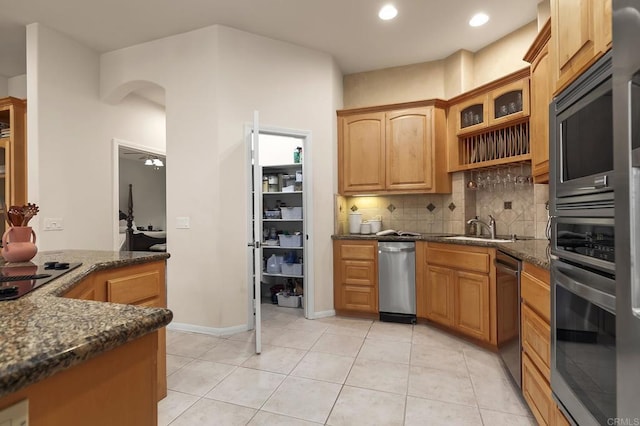 kitchen with light tile patterned flooring, appliances with stainless steel finishes, a sink, dark stone counters, and tasteful backsplash