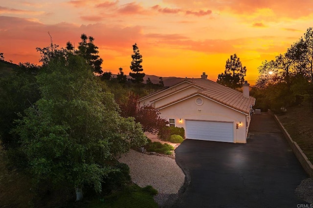 view of front of house with a garage, stucco siding, a chimney, driveway, and a tile roof