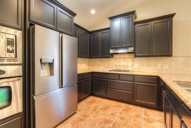 kitchen with recessed lighting, under cabinet range hood, tasteful backsplash, light stone counters, and stainless steel appliances
