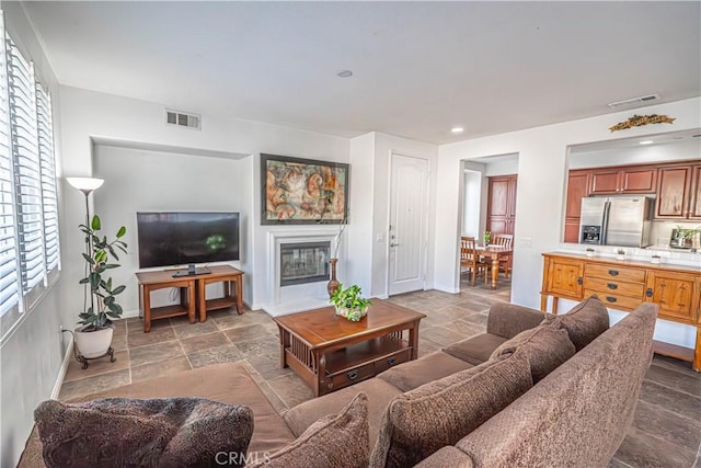 living room with baseboards, visible vents, a wealth of natural light, and stone tile floors