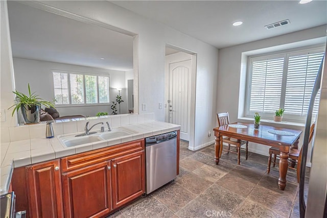 kitchen featuring tile countertops, stone finish flooring, visible vents, dishwasher, and a sink