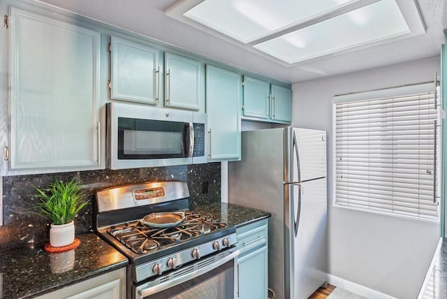 4658 Ohio St, San Diego, CA 92116 - kitchen featuring appliances with stainless steel finishes, backsplash, dark stone countertops, blue cabinetry, and baseboards