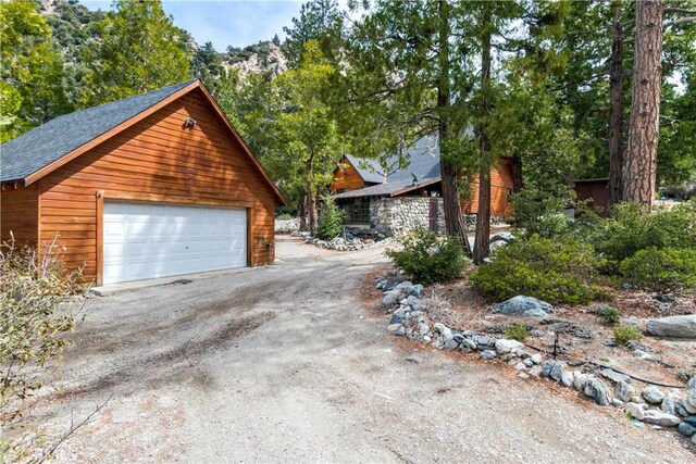 view of side of home featuring a detached garage, an outdoor structure, and roof with shingles