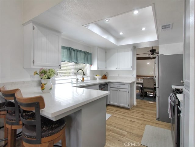kitchen featuring ceiling fan, stainless steel range with gas stovetop, a peninsula, light wood-style floors, and a tray ceiling