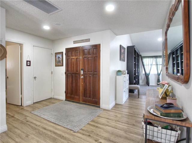 entryway featuring a textured ceiling, recessed lighting, baseboards, wood finished floors, and visible vents