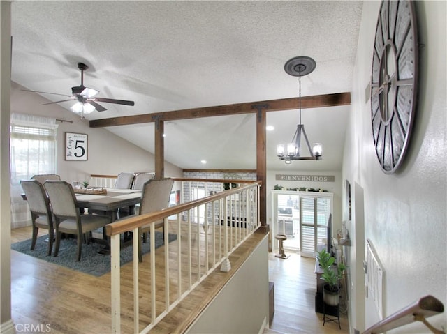 interior space with a textured ceiling, lofted ceiling with beams, wood finished floors, and ceiling fan with notable chandelier
