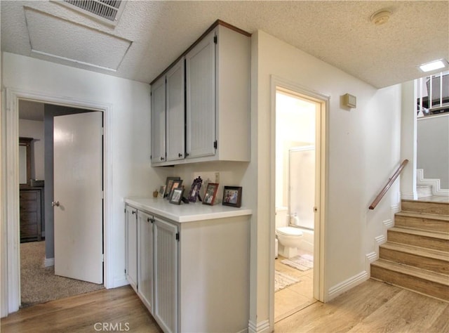 interior space with light wood-style floors, stairway, a textured ceiling, and visible vents