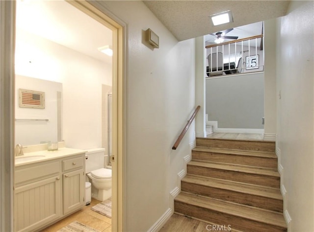 staircase featuring baseboards, ceiling fan, and wood finished floors