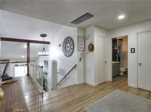 hallway with visible vents, a textured ceiling, wood finished floors, and an upstairs landing