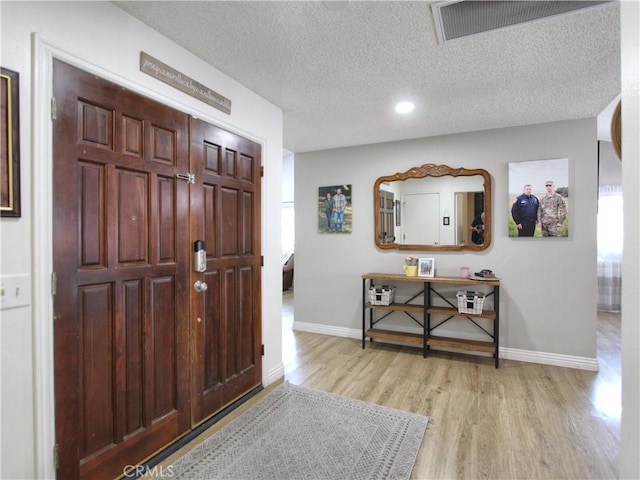 foyer entrance featuring light wood-style floors, baseboards, a textured ceiling, and visible vents