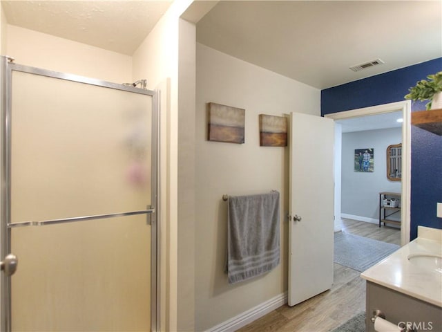 full bath featuring visible vents, a stall shower, wood finished floors, vanity, and baseboards