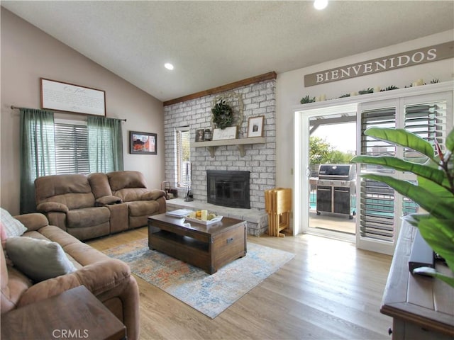 living room with a fireplace, a textured ceiling, recessed lighting, wood finished floors, and lofted ceiling