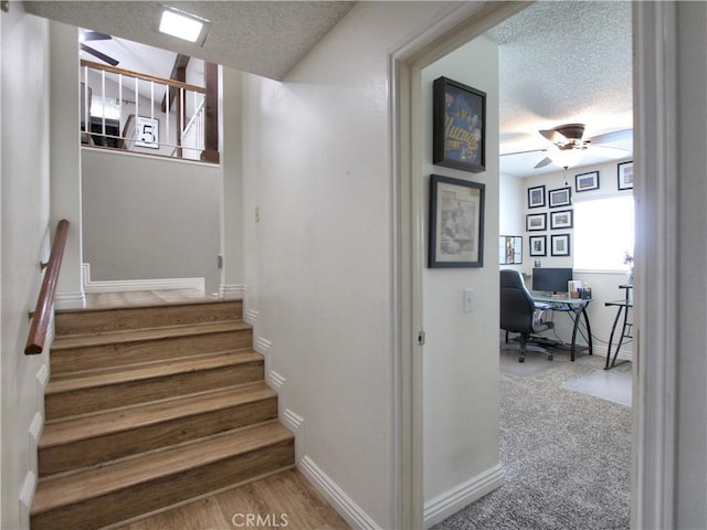 staircase featuring baseboards, ceiling fan, and a textured ceiling