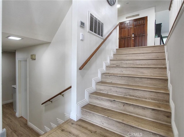 stairway with baseboards, wood finished floors, and visible vents