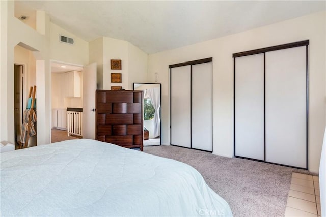 bedroom with visible vents, multiple closets, carpet floors, and vaulted ceiling