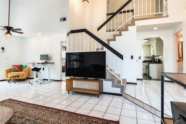 living area featuring ceiling fan, light tile patterned floors, a towering ceiling, visible vents, and stairway
