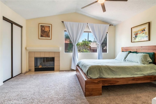 bedroom with a ceiling fan, a tiled fireplace, vaulted ceiling, carpet floors, and a closet