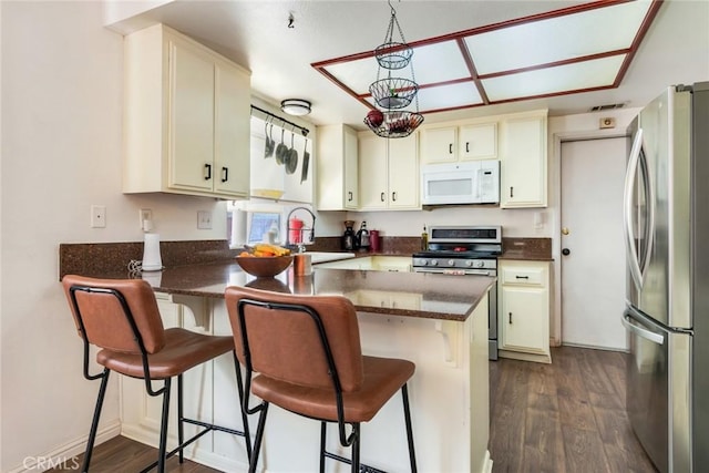 kitchen featuring a sink, appliances with stainless steel finishes, dark wood-style flooring, and a peninsula