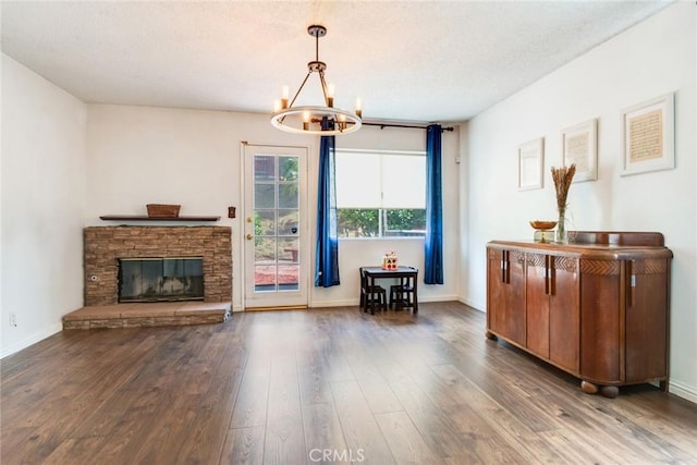 interior space with an inviting chandelier, a textured ceiling, a stone fireplace, baseboards, and wood finished floors