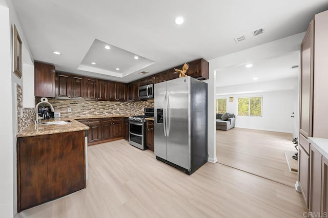 kitchen with appliances with stainless steel finishes, tasteful backsplash, a sink, a raised ceiling, and recessed lighting