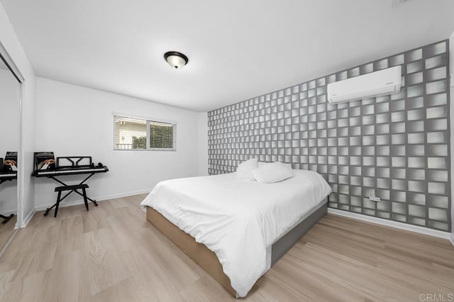 bedroom with wood finished floors, baseboards, a wall unit AC, and a closet