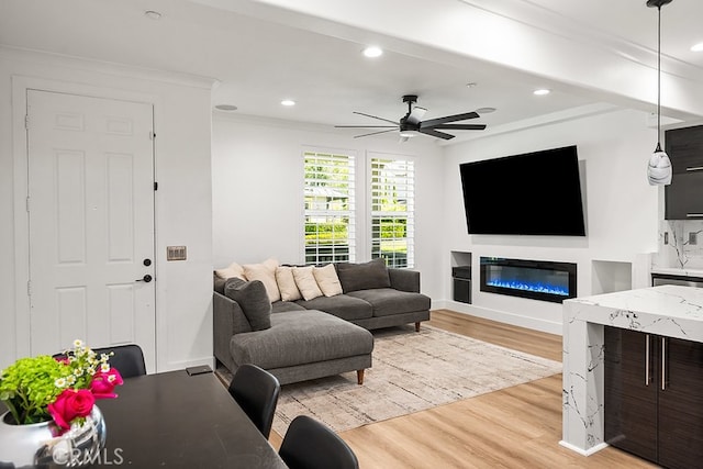 living area featuring light wood-style floors, a ceiling fan, a glass covered fireplace, and recessed lighting