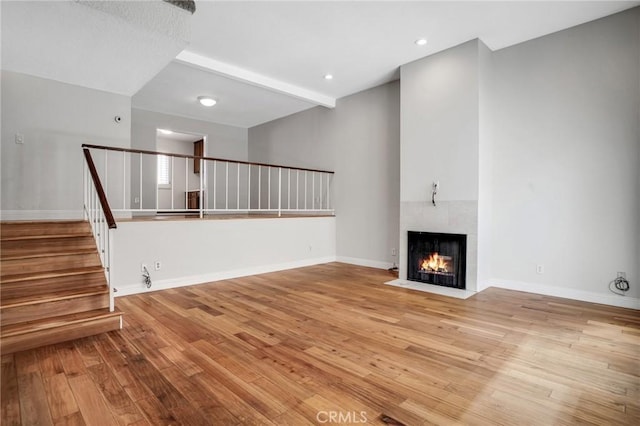 unfurnished living room with stairway, baseboards, a fireplace, and hardwood / wood-style flooring