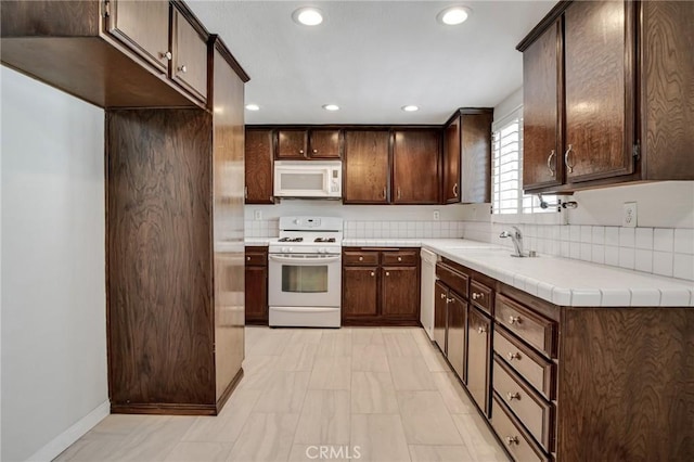 kitchen featuring white appliances, recessed lighting, dark brown cabinetry, and a sink