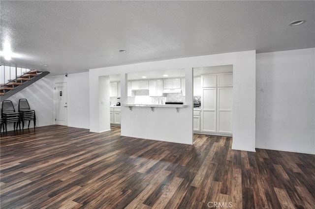 unfurnished living room featuring dark wood finished floors, a textured ceiling, and stairs