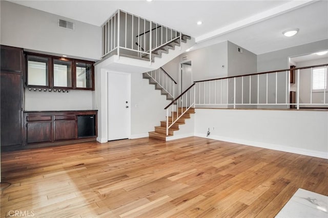 unfurnished living room with hardwood / wood-style flooring, baseboards, stairs, and visible vents